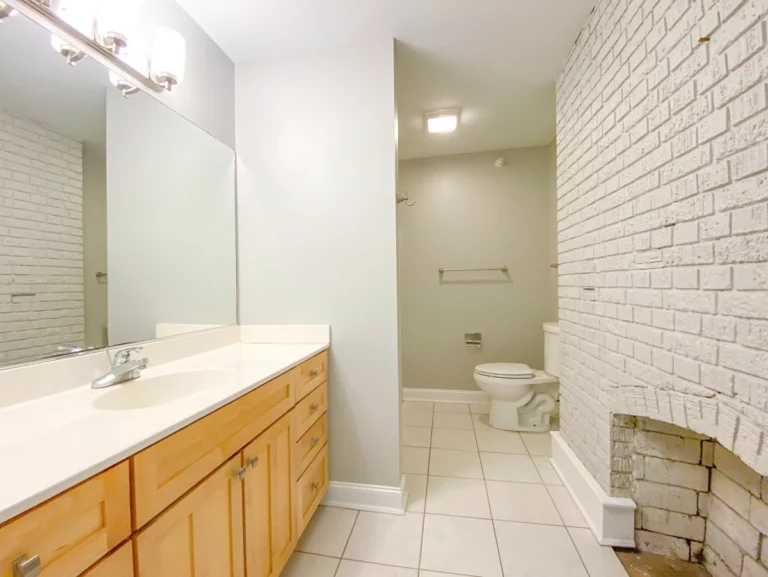 A photograph of a bathroom with a white-painted brick fireplace along a wall opposite of the sink.