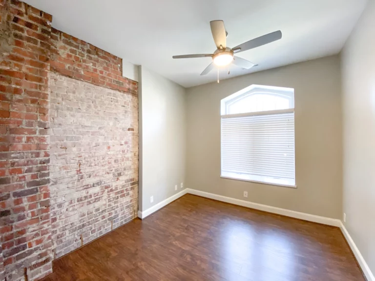 A bedroom with wood floors and exposed brick on a portion of wall.