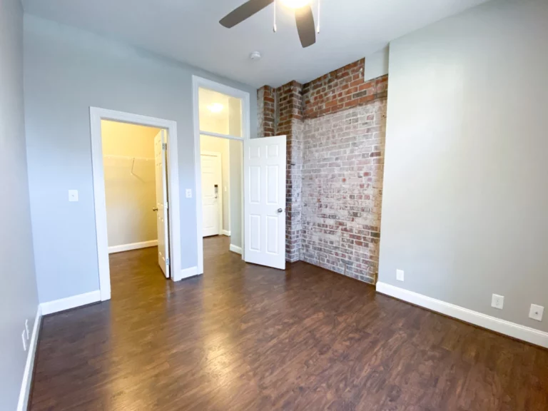 A bedroom with wood floors, a walk-in closet, and a section of exposed brick on a wall.