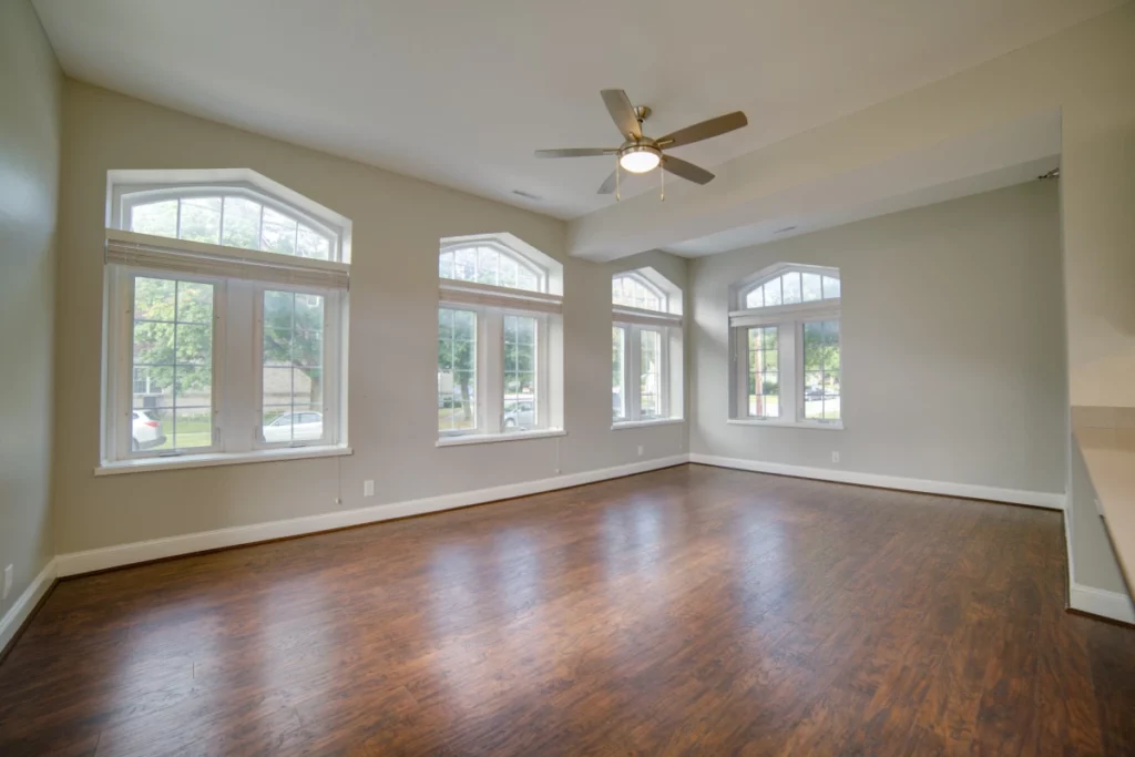 An apartment living room with wood floors and four large windows.